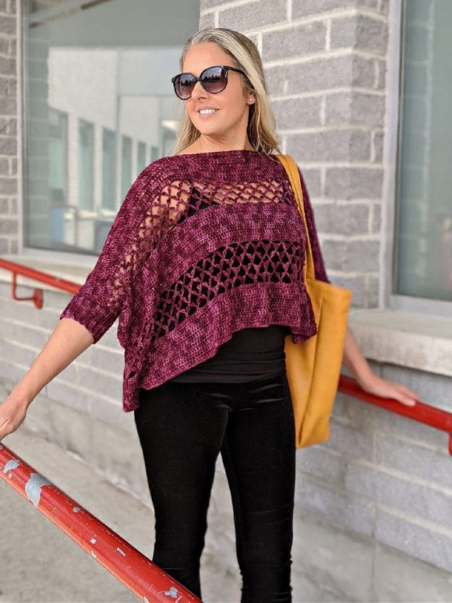 Contessa Cropped Pullover by Sincerely Pam. A model wears a plum-colored cropped pullover topped with openwork crochet mesh. She's holding a bright yellow tote bag and wearing sunglasses.