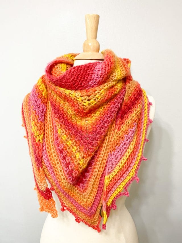 Atlantic Waves Shawl by Stitch & Hustle. A sunset-colored crocheted shawl draped on a dress form.