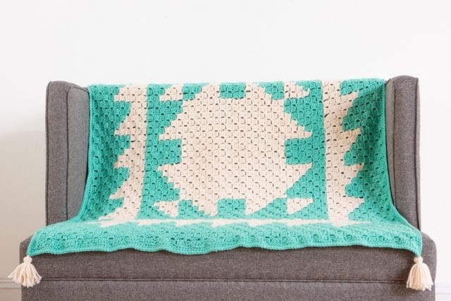 A corner to corner crocheted blanket draped on a couch.