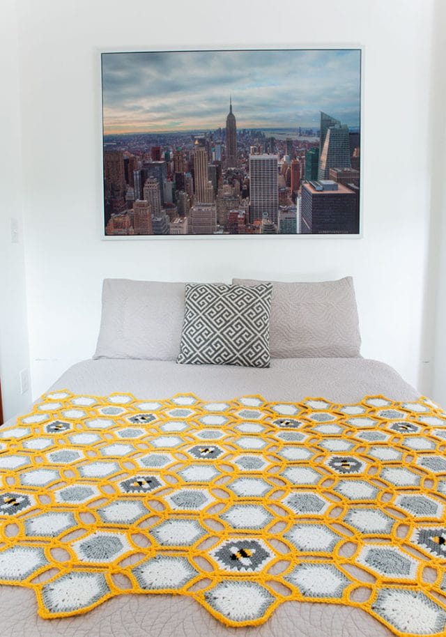 A cheerful yellow and gray blanket spread on a bedspread. It's punctuated with hexagons featuring a bee motif.