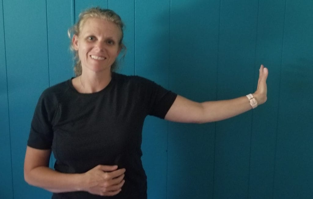 An image of a woman demonstrating a crochet stretch: stretching her arm out to the side with her hand reaching back.