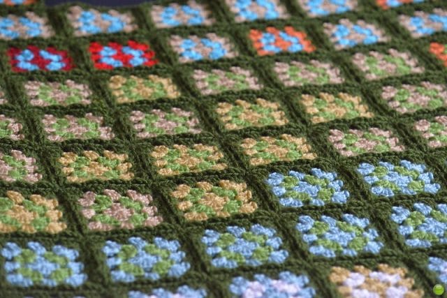 A sweeping view of a granny square blanket made temperature-style, with a dark green backing, and alternating inner colors for each granny square. Inspiration for crocheting a temperature blanket.