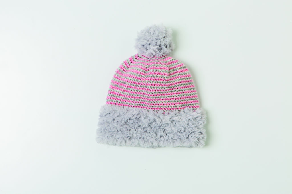 The Brava Beanie, a striped crocheted beanie with a fur pom-pom