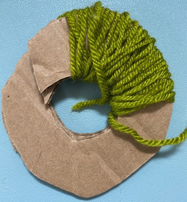 10 Thrifty Crochet Tips from the WeCrochet Blog at crochet.com. This photo shows: a cardboard circle being used as a pom-pom maker.