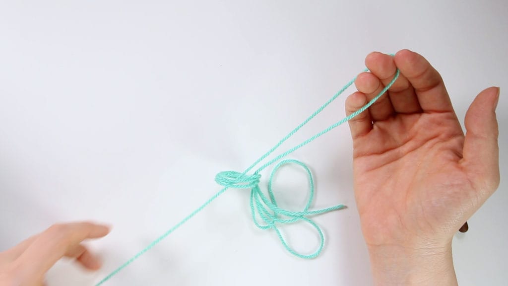 Pick up the single strand of yarn coming from cake or skein, and pull it through loop. This image shows the loop being pulled through.