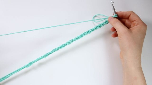 Hands crocheting a long crochet chain.