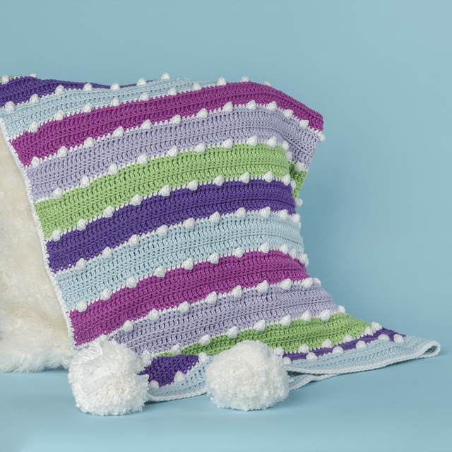 Holiday lights blanket shown draped over a fur pillow, a free crochet pattern from crochet.com