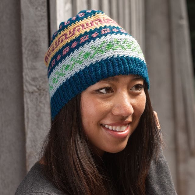 A model wears a multicolored crocheted hat: The Multiverse Colorwork Cap by WeCrochet at crochet.com