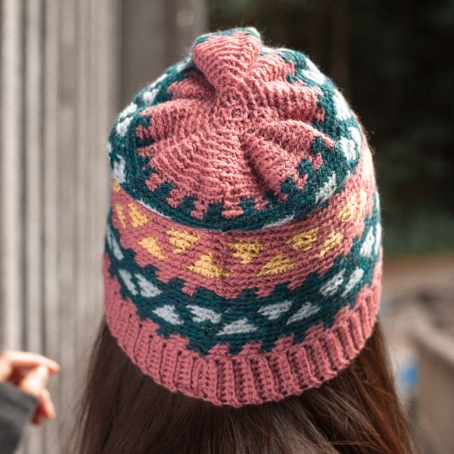 (back view) A model wears a multicolored crocheted hat: The Multiverse Colorwork Cap by WeCrochet at crochet.com