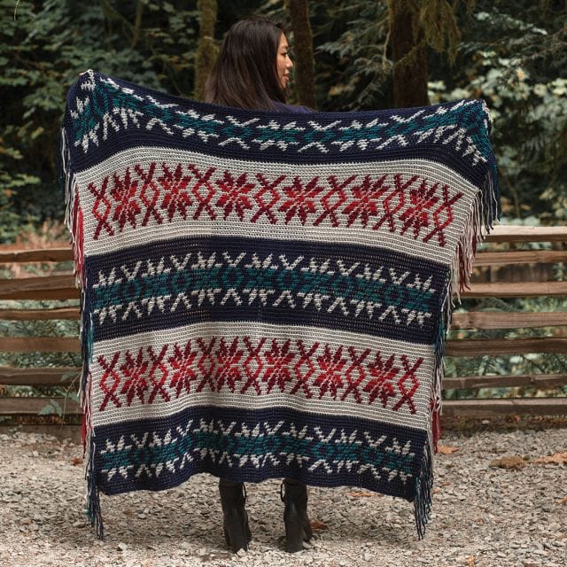 A woman holds up a crocheted blanket with a Nordic snowflake motif