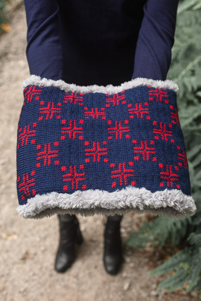 Hands hold a crocheted cowl with a navy background and red geometric pattern. A fun and challenging winter crochet pattern.