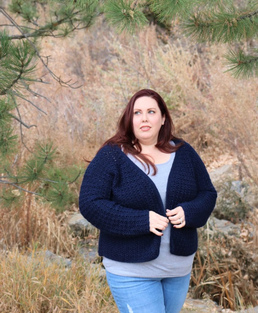 A model wears the Amaretti Boyfriend Cardigan, a navy blue crochet cardigan by Crochet Foundry