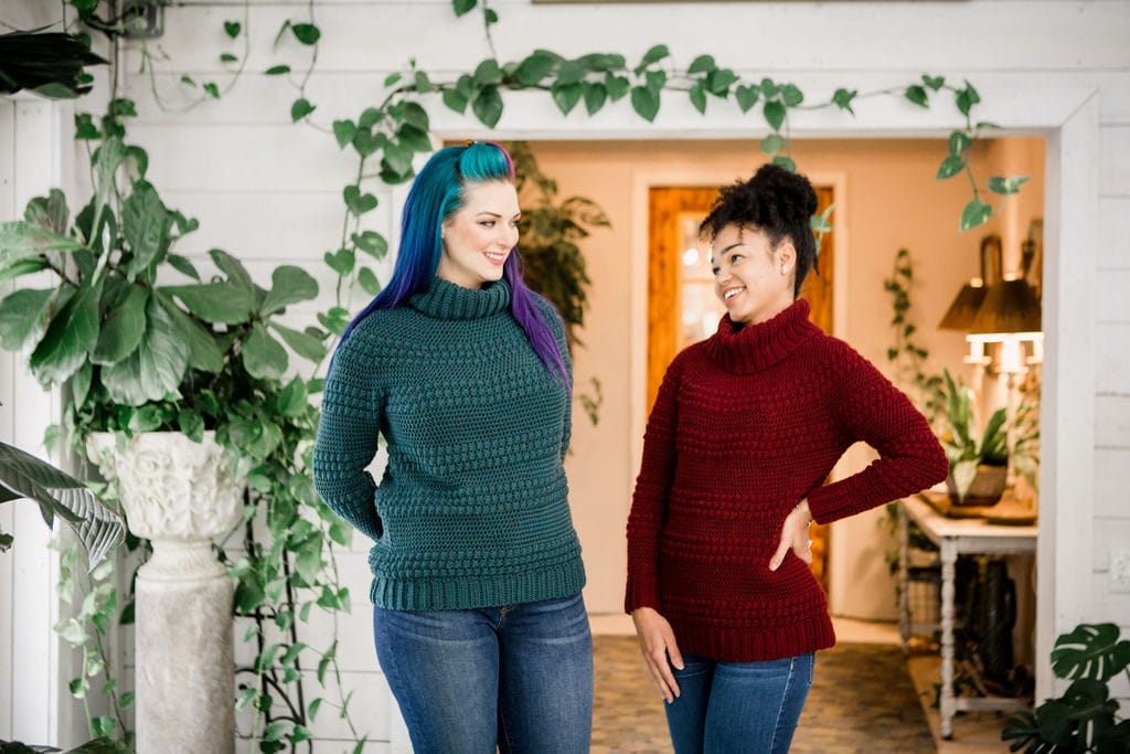 Two models wear the Cranberry Biscotti Turtleneck, a crocheted sweater by Crochet Foundry