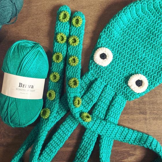 A turquoise crocheted octopus scarf next to a ball of Brava yarn