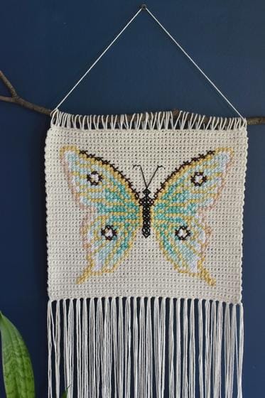 Crocheted wall hanging featuring a butterfly on a cream-colored background with long fringe