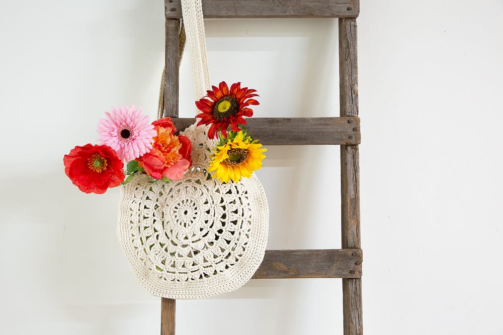 A crocheted bag with a round mandala motif, filled with flowers