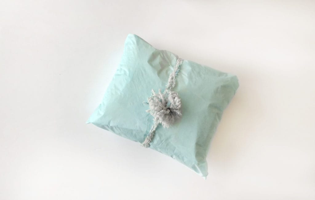 Making a pom-pom package topper with yarn: a top-down view of a mint green package with a fur pom pom tied around it