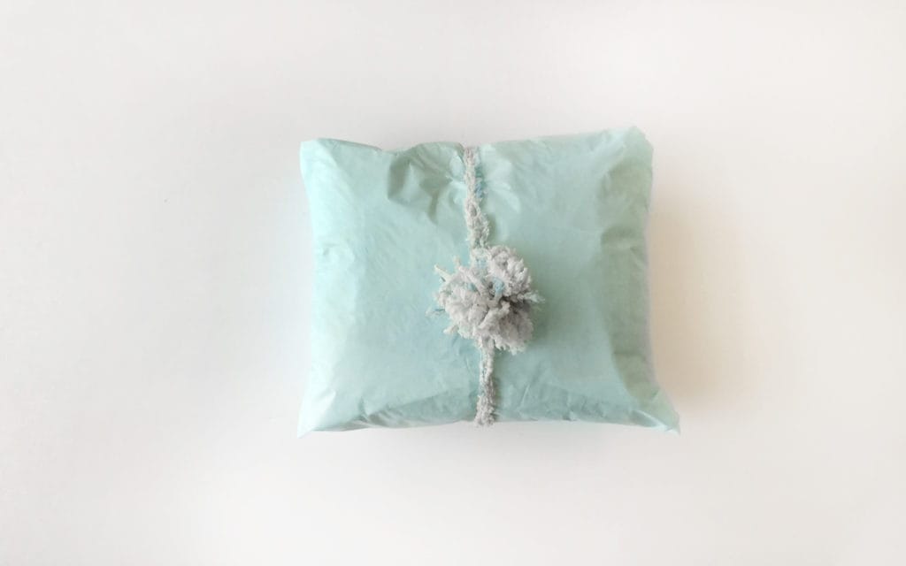 Making a pom-pom package topper with yarn: a top-down view of a mint green package with a fur pom pom tied around it