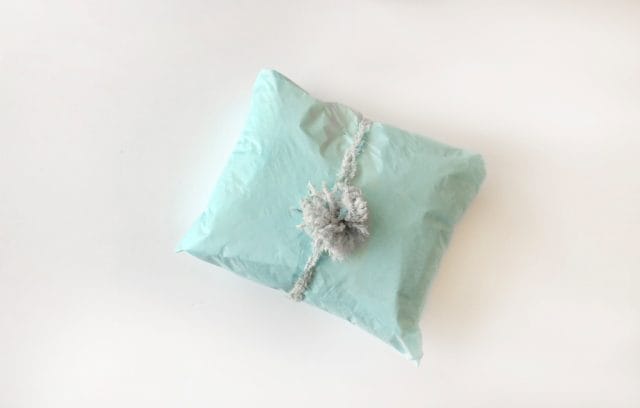 Making a pom-pom package topper with yarn: a top-down view of a mint green package with a fur pom pom tied around it