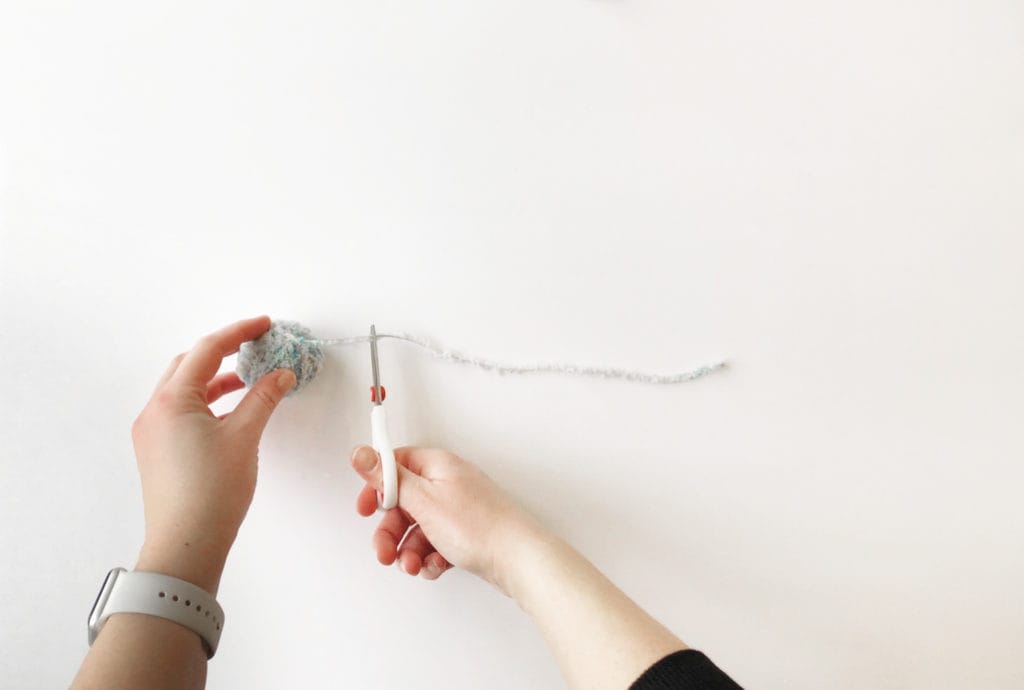 Hands cutting a 12" piece of fur yarn to tie the pom pom