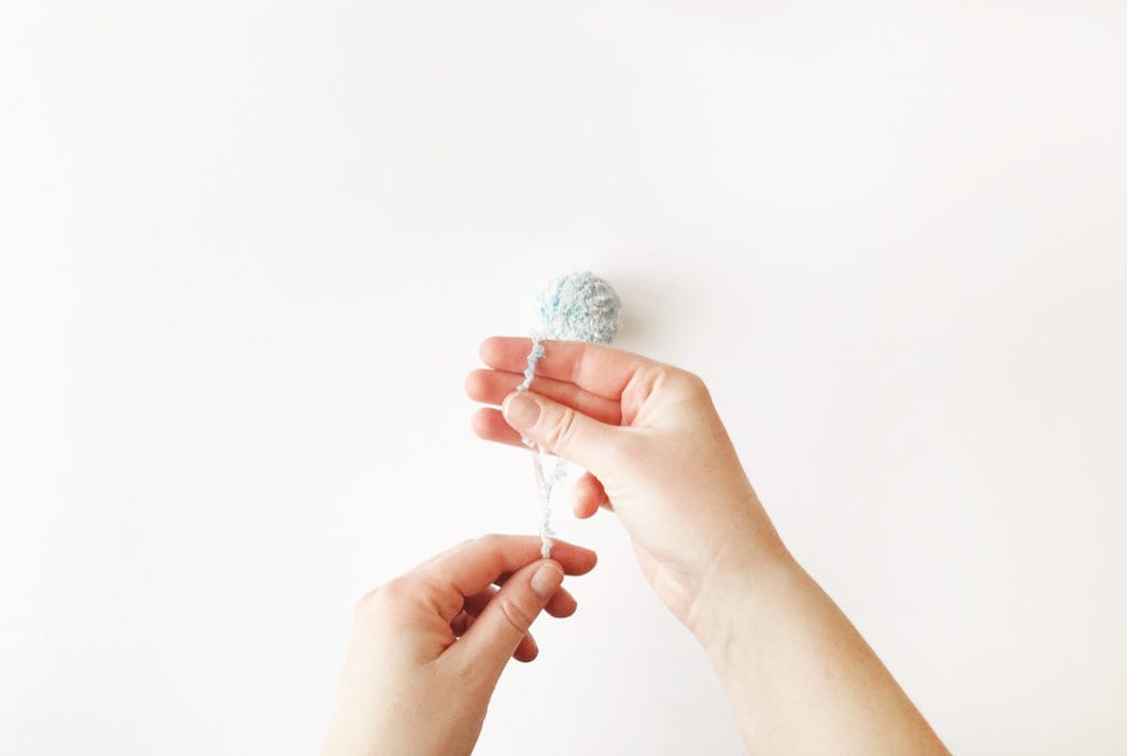 A top-down shot of hands wrapping fur yarn around 3 fingers to make a pom-pom