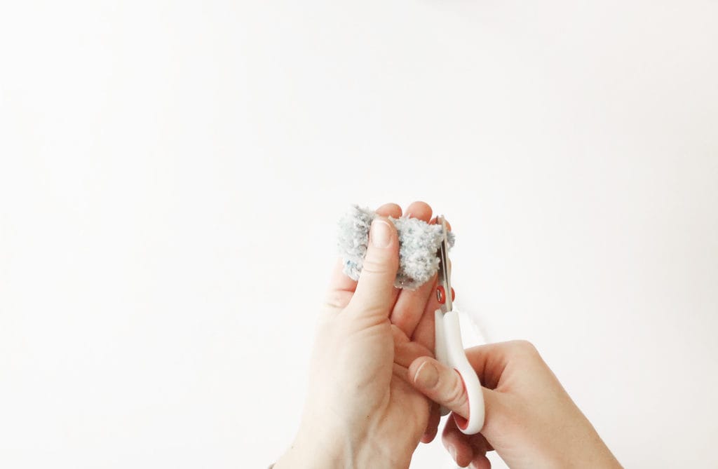 Hands trimming a handmade pom-pom made of fur yarn