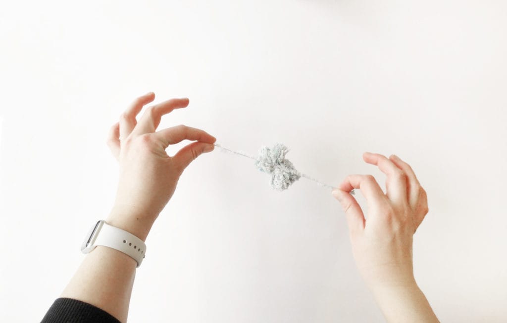 Hands tying a handmade pom-pom made of fur yarn