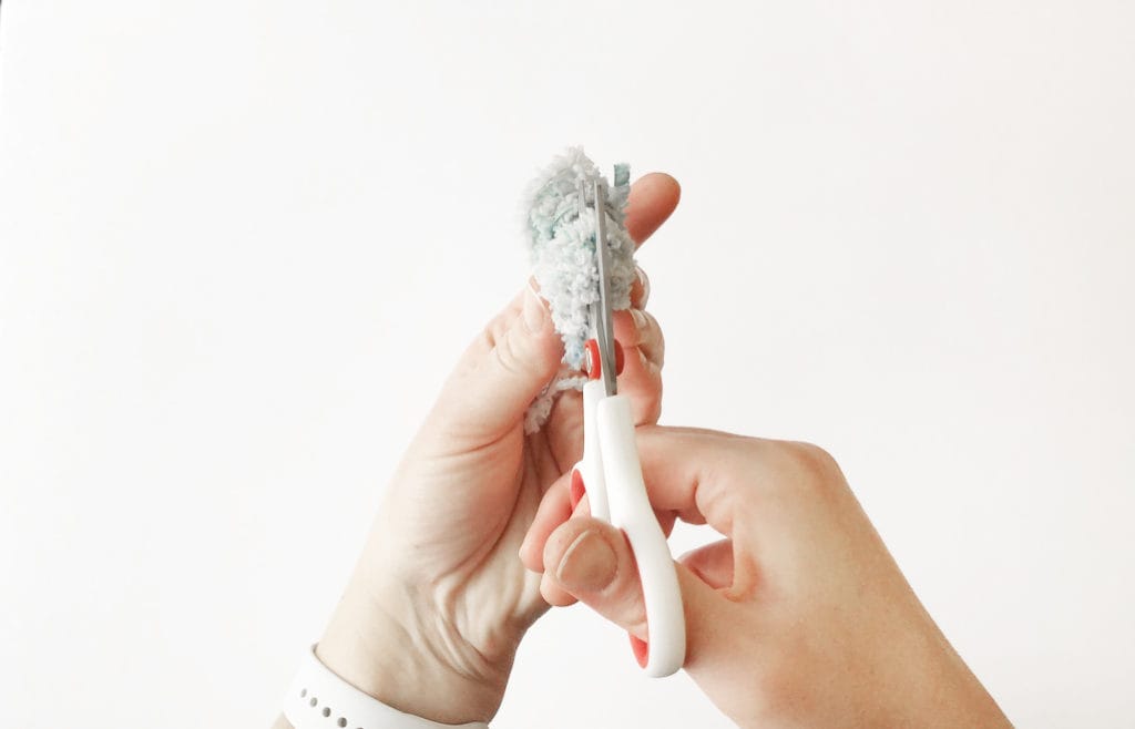 Hands cutting a handmade pom pom made from fur yarn