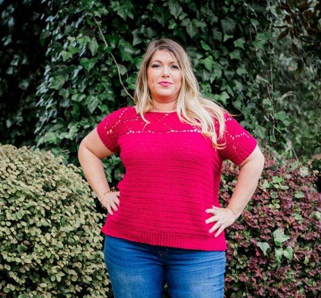 Riviera Tee: A woman wears a fuchsia crocheted t-shirt sweater with a leaf motif across the top yoke and short sleeves, and a solid body and ribbed waistband that falls at her hip.