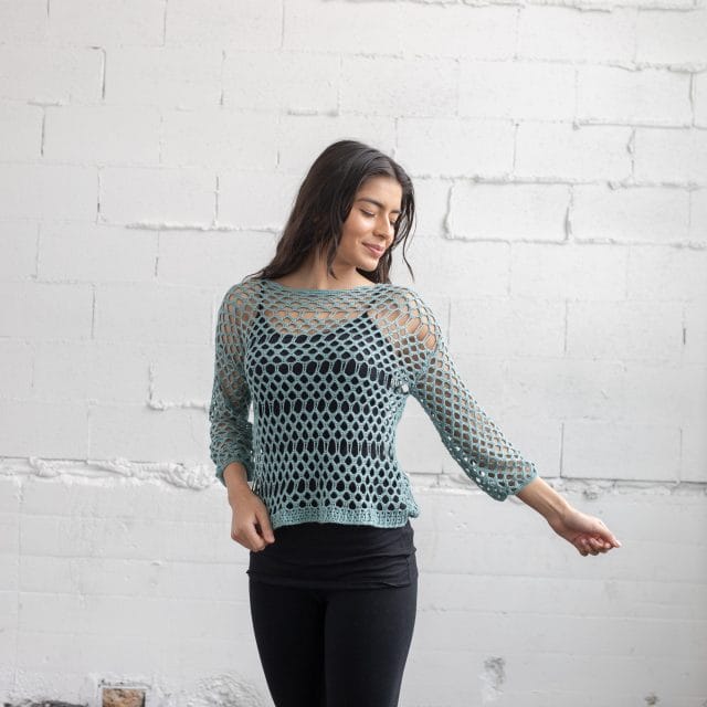 Delicato top: a woman wears a hand-crocheted pullover in large openwork mesh.