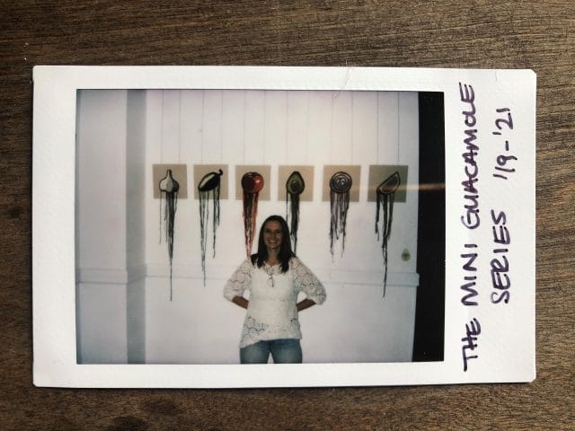 A polaroid photo featuring Kate Moran standing in front of the mini versions of her guacamole art pieces
