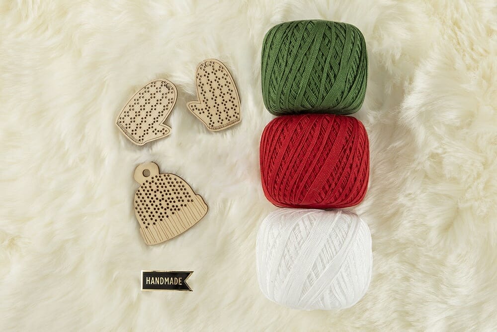 A fur background with 3 wooden ornaments and 3 balls of yarn and an enamel pin