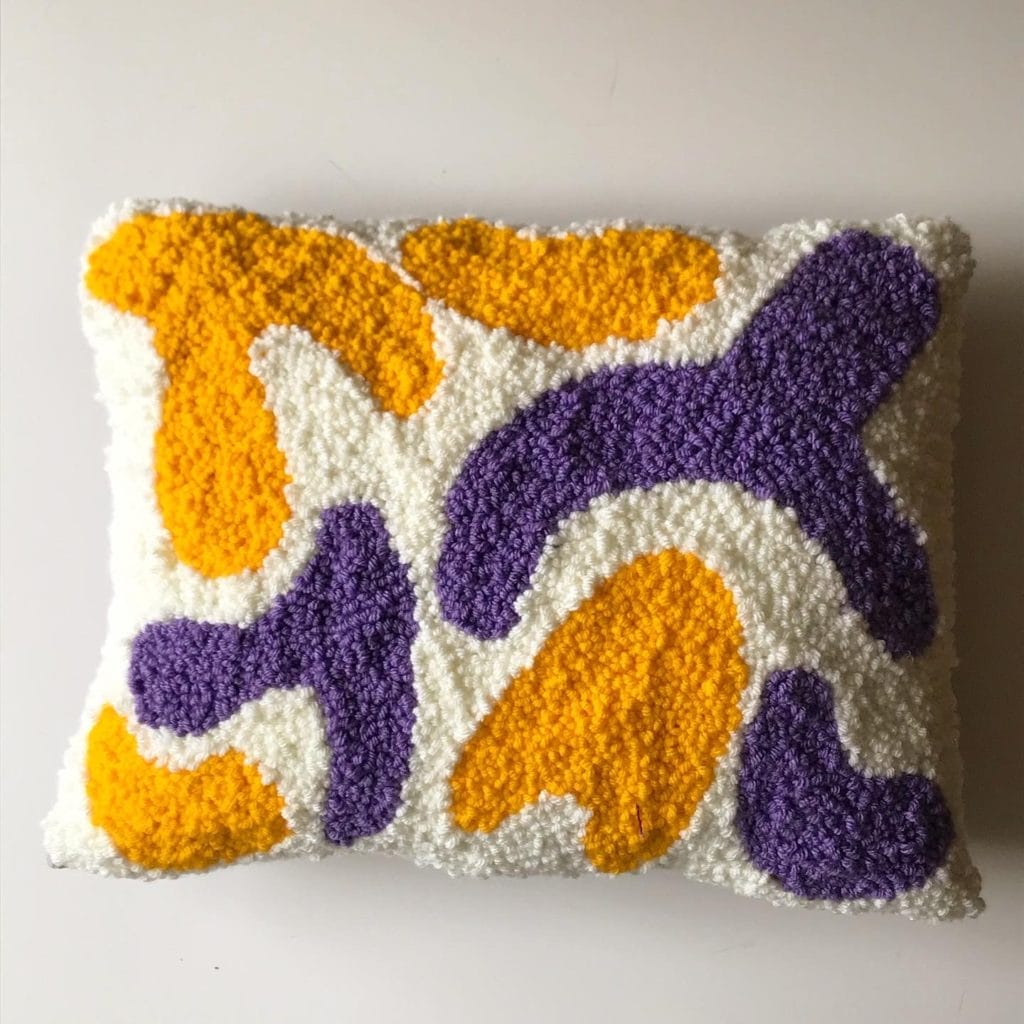 One of Liz's punch needle projects. An abstract design of yellow and purple shapes on a cream-colored background
